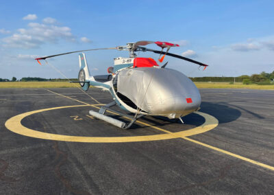 H130 Airbus Helicopter with reflective cover and blade tip socks on a runway in sunny weather.