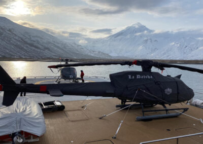 H125 Airbus helicopter in full black protective cover set, on a yacht in a snowy, icy environment.
